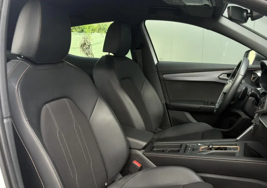 Vue intérieure côté conducteur du CUPRA Formentor 2025, sièges sports noirs avec surpiqûres et accoudoir central réglable.