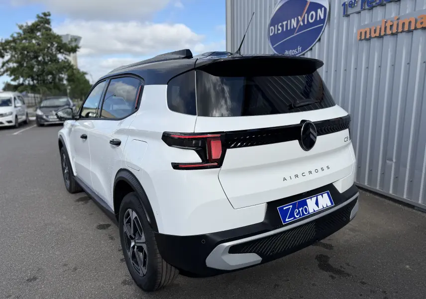Vue 3/4 arrière droite d'une Citroën C3 Aircross blanc banquise avec toit noir, feux arrière LED et logo central noir.