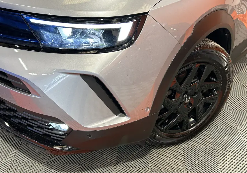 Gros plan sur l'avant droit gris de l'Opel Mokka GS Line 2022, mettant en valeur le phare LED et la jante noire brillante.