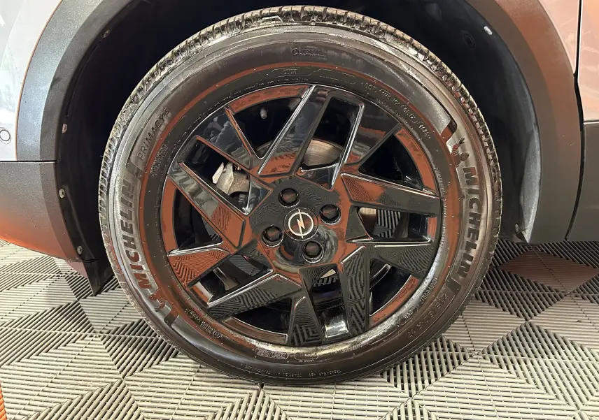 Gros plan sur la roue avant droite noire brillante de l'Opel Mokka gris avec pneu Michelin visible.