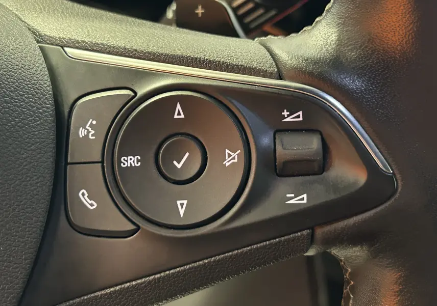 Gros plan sur les commandes noires du volant côté gauche de l’Opel Mokka gris, avec boutons de volume et appels.