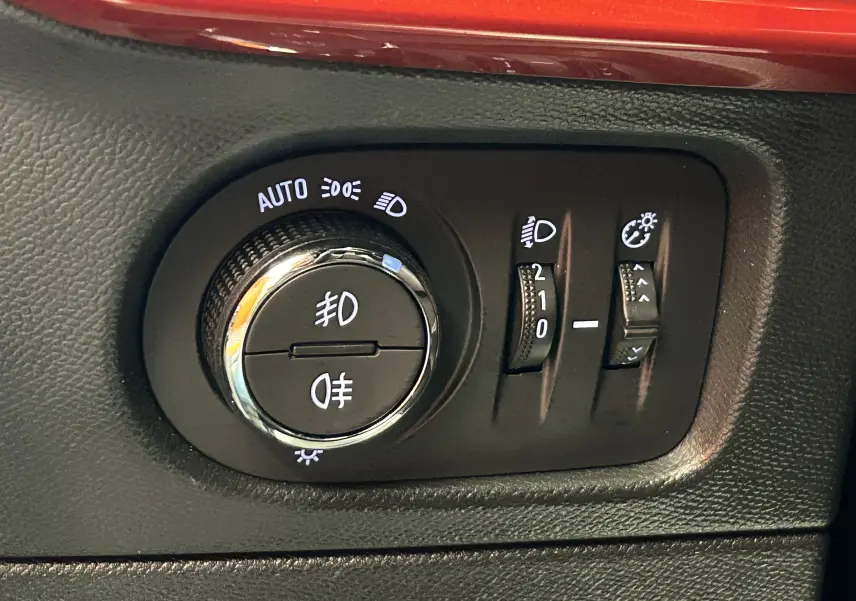 Gros plan sur les commandes d’éclairage et réglages de phares du tableau de bord noir d’un Opel Mokka gris.