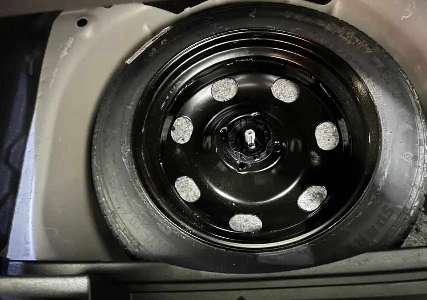 Gros plan sur la roue de secours noire dans le coffre d’un Opel Mokka gris, vue plongeante depuis l’arrière.