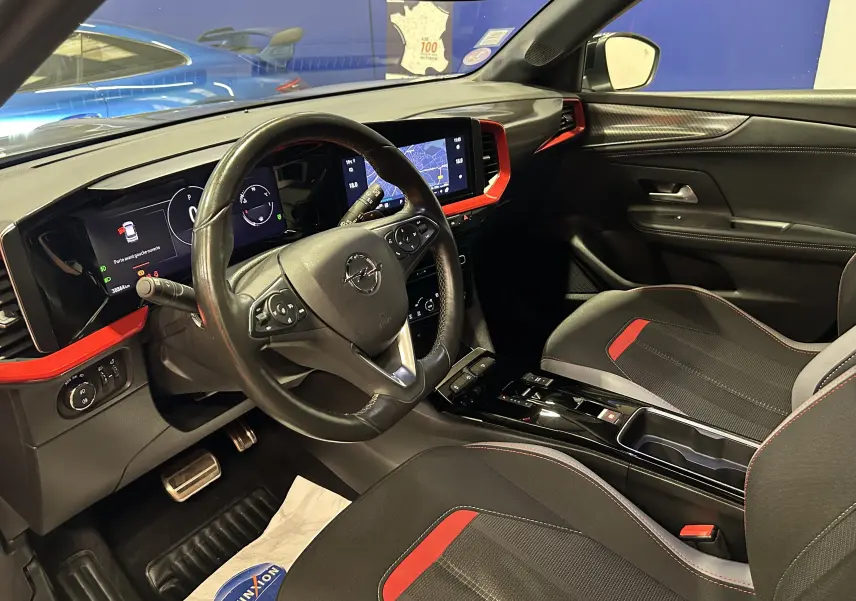 Vue intérieure côté conducteur de l’Opel Mokka GS Line avec sièges noirs et rouges et tableau de bord moderne avec écran tactile.