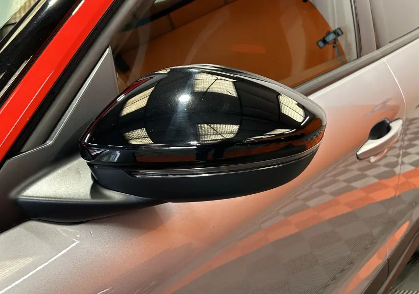 Gros plan sur le rétroviseur noir brillant côté gauche d'un Opel Mokka gris avec reflet de lumière intérieure.