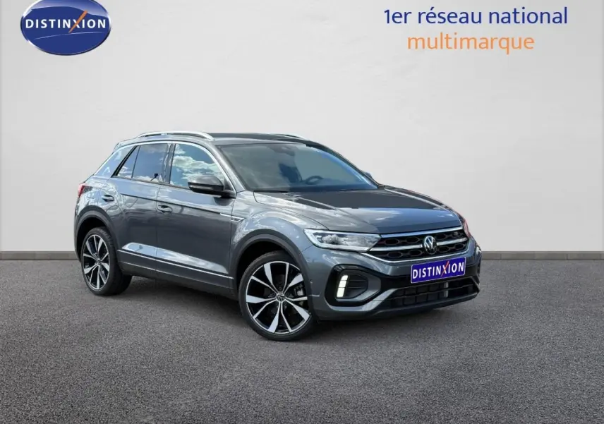 Volkswagen T-Roc gris Indium métallisé en 3/4 avant droit, avec jantes alliage et barres de toit visibles.