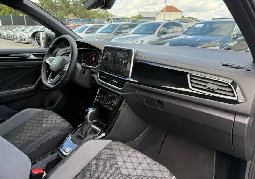 Vue intérieure avant droite du Volkswagen T-Roc 2025 avec sellerie gris artvelours et tableau de bord noir brillant.
