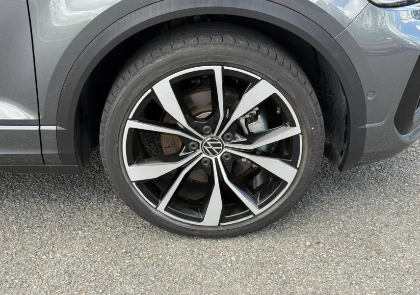 Gros plan sur la roue avant droite du Volkswagen T-Roc gris Indium métallisé avec jante alliage noire et argentée.