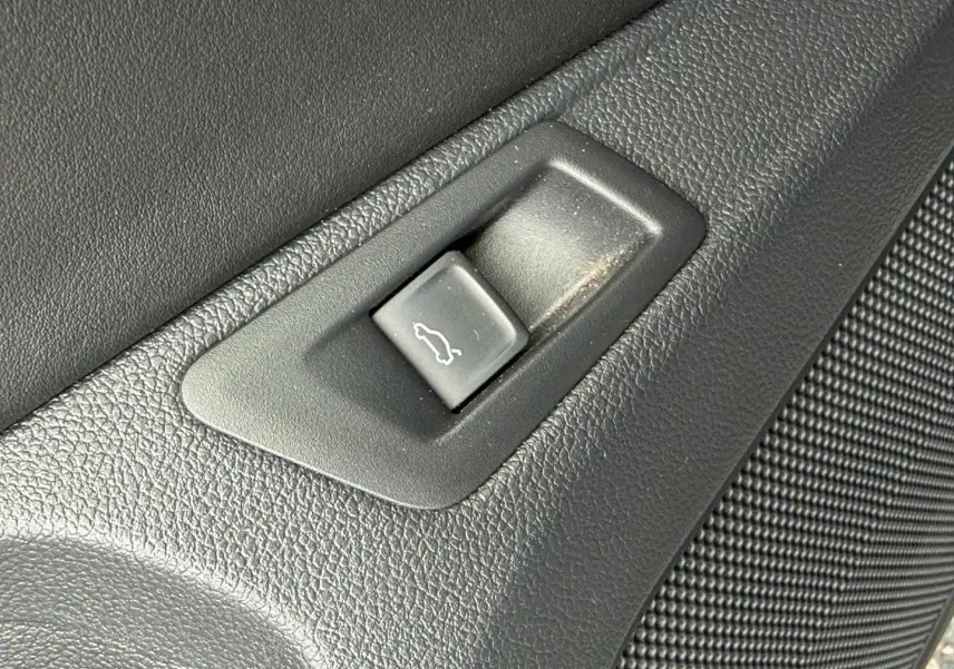Bouton d'ouverture du coffre en plastique noir sur panneau intérieur texturé d'un Volkswagen T-Roc gris Indium.