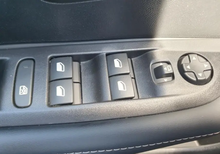 Gros plan sur les commandes de lève-vitres et réglage des rétroviseurs côté conducteur d'une Peugeot 208 1.2 Hybrid 110 gris Sellenium.