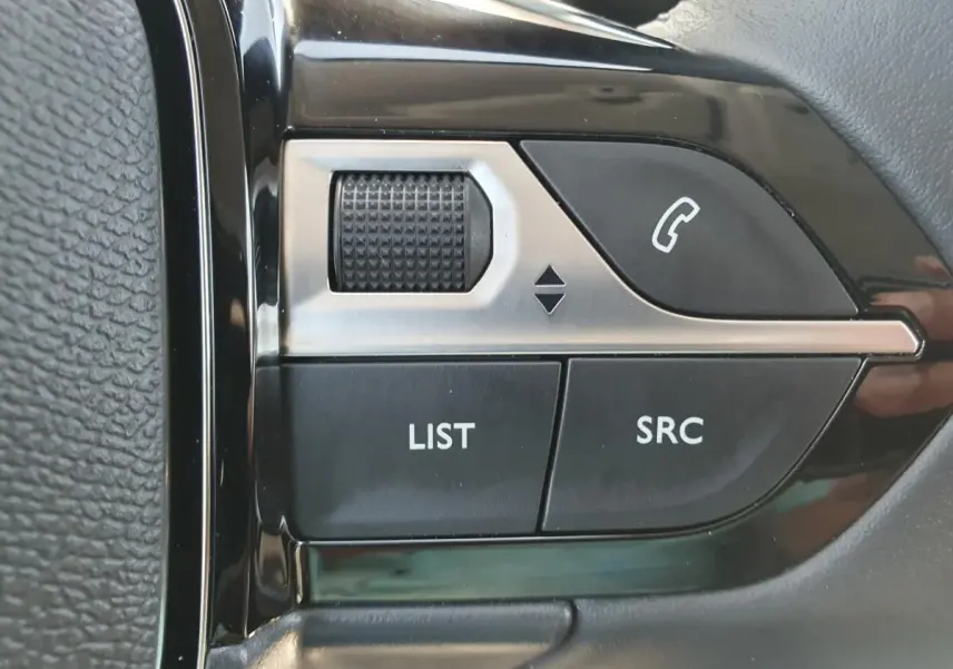 Gros plan sur les commandes multimédia au volant côté gauche du Peugeot 208 gris Sellenium 2025.