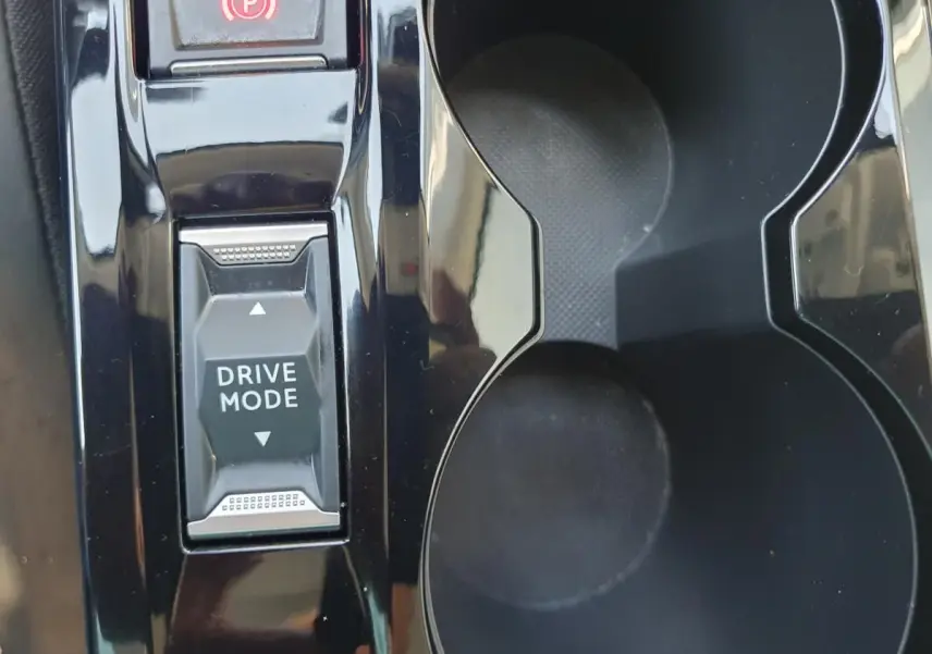 Gros plan sur la console centrale noire brillante de la Peugeot 208 1.2 Hybrid avec bouton Drive Mode et porte-gobelets.