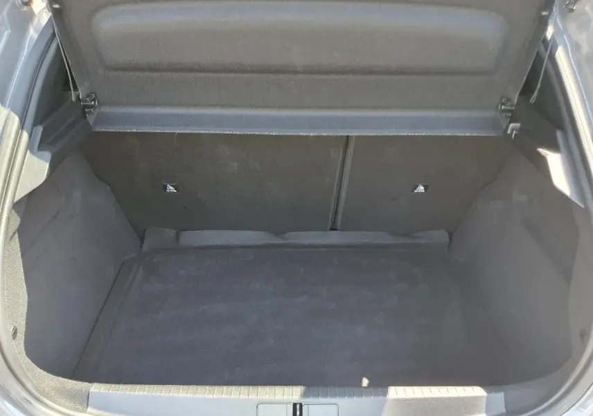 Coffre ouvert de la Peugeot 208 gris Sellenium, vue plongeante montrant l'espace de chargement vide et la moquette noire.