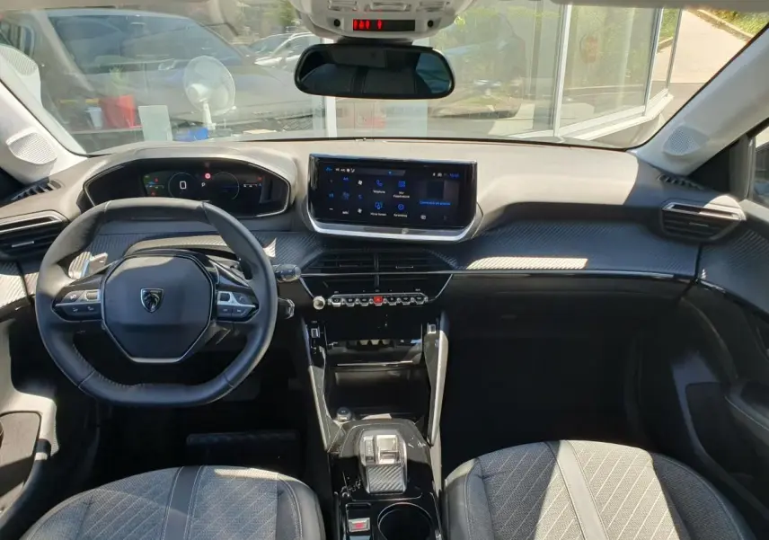 Vue intérieure avant de la Peugeot 208 1.2 Hybrid 110 Allure, tableau de bord noir avec écran tactile 10 pouces.