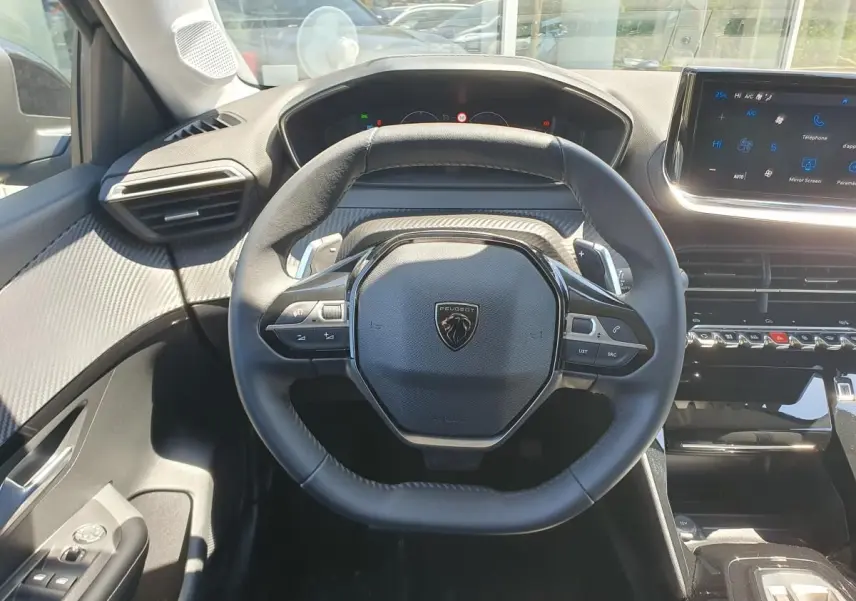 Vue intérieure centrée sur le volant cuir noir et le tableau de bord moderne de la Peugeot 208 1.2 Hybrid 110 Allure.