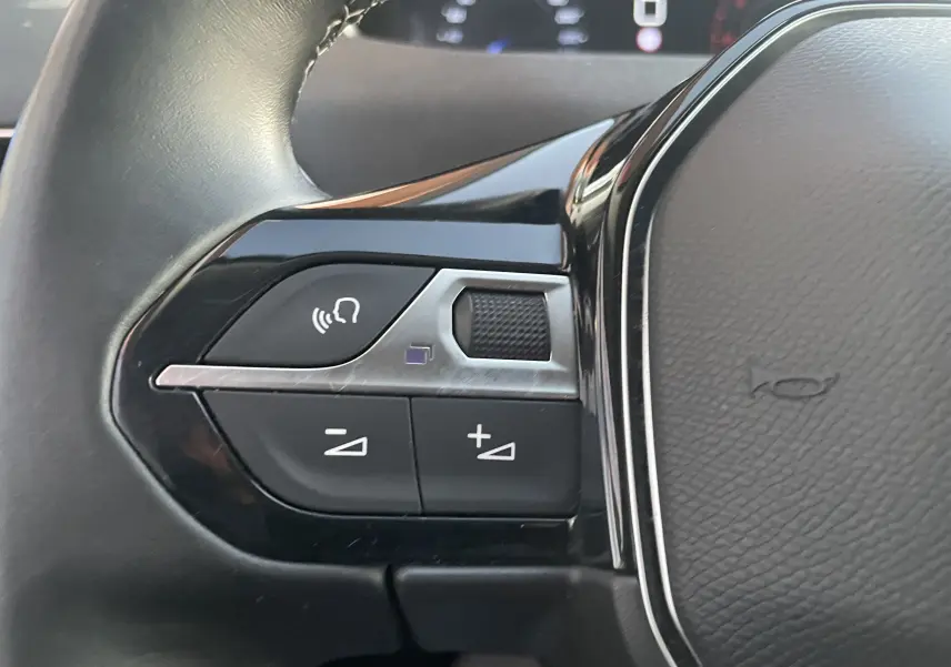 Gros plan sur les commandes du volant côté gauche du Peugeot 3008 blanc nacré, version 2019 avec boutons de volume et commande vocale.