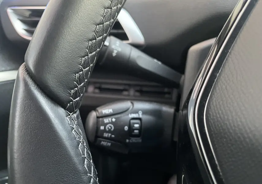 Gros plan sur la commande de régulateur de vitesse derrière le volant noir du Peugeot 3008 blanc nacré, version 2019.