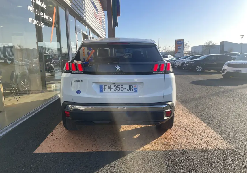 Vue arrière d'un Peugeot 3008 blanc nacré garé devant un showroom, avec ses feux arrière LED caractéristiques allumés.
