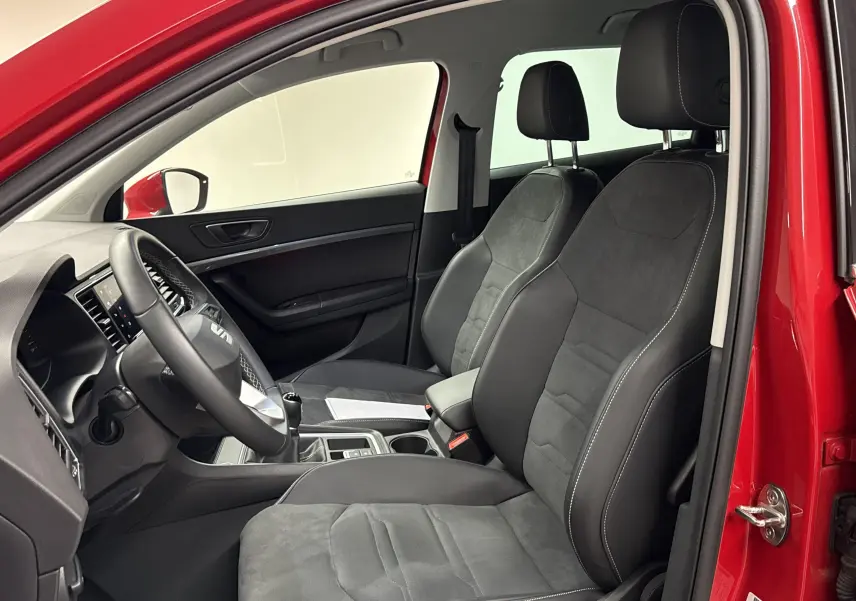 Vue intérieure côté conducteur du SEAT Ateca 2024 Rouge Velvet, sièges en cuir et alcantara avec volant et levier de vitesses manuels.