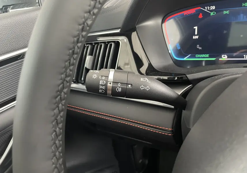 Gros plan sur la manette de commande des phares et clignotants dans l’habitacle noir avec surpiqûres rouges du BYD SEAL U hybride rechargeable.