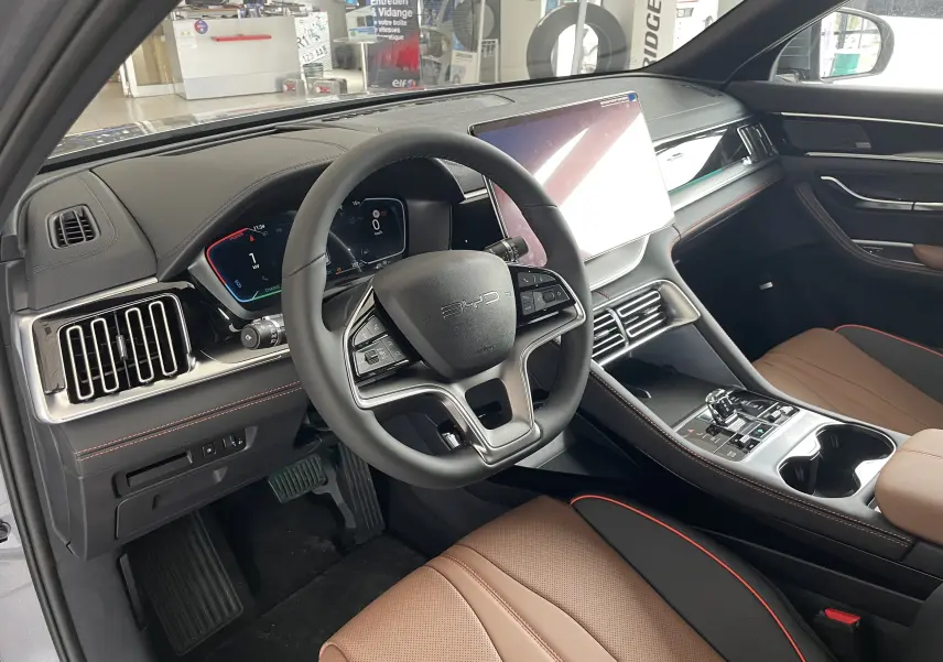 Vue intérieure avant droite du BYD SEAL U 2026 avec tableau de bord noir, écran tactile 15,6'', et sièges marron avec surpiqûres rouges.