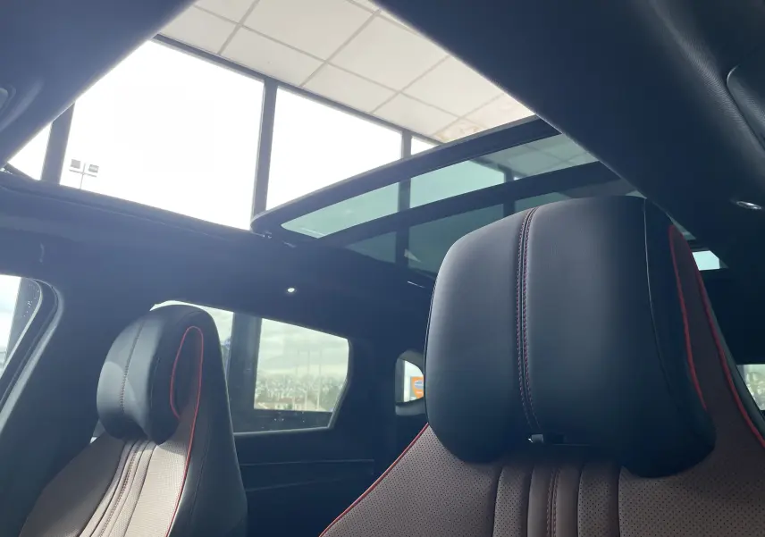 Vue intérieure sur les sièges avant en similicuir noir et brun avec surpiqûres rouges, toit ouvrant panoramique ouvert.
