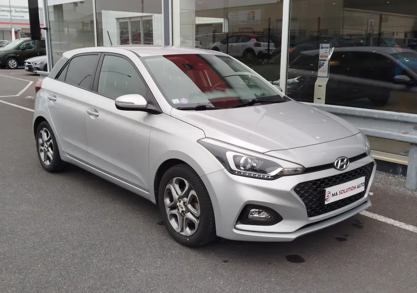 Vue 3/4 avant gauche d'une Hyundai i20 2018 gris argent métallisé avec jantes alliage et calandre noire distinctive.