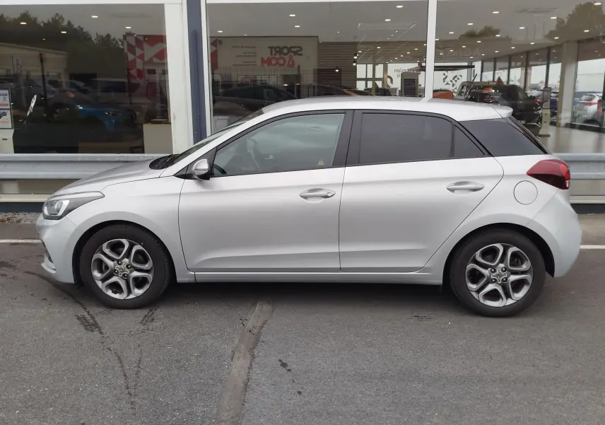 Vue de profil côté gauche d'une Hyundai i20 2018 gris argenté, avec vitres teintées et jantes alliage distinctives.