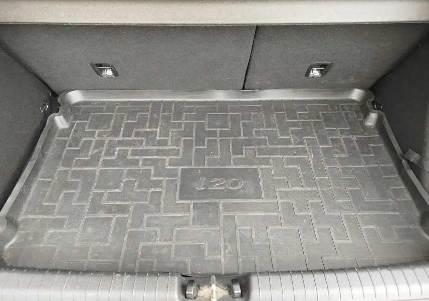 Vue intérieure du coffre d'une Hyundai i20 avec tapis de sol en caoutchouc noir marqué "i20" au centre.