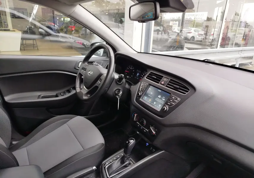Vue intérieure côté conducteur de la Hyundai i20 2018, avec tableau de bord gris et écran tactile central.