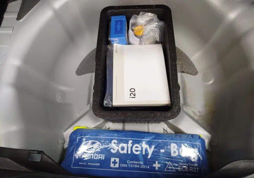 Coffre à roue de secours d’une Hyundai i20 2018 avec trousse de sécurité bleue et manuel du véhicule visible.