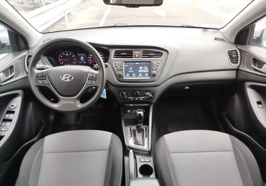 Vue intérieure avant de la Hyundai i20 2018 en gris, montrant le tableau de bord, volant multifonction et console centrale avec écran tactile.