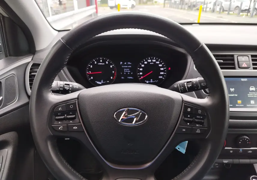 Vue intérieure centrée sur le volant noir de la Hyundai i20 2018, avec tableau de bord et écran tactile visibles.