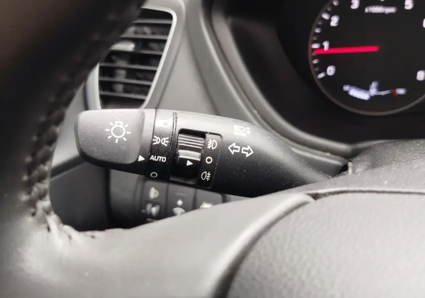 Gros plan sur la manette des feux et clignotants à gauche du volant d’une Hyundai i20 gris intérieur, avec tableau de bord partiellement visible.