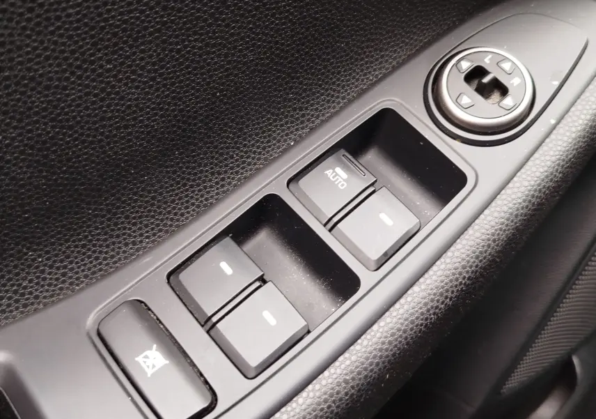 Gros plan sur les commandes de lève-vitres et réglage des rétroviseurs côté conducteur d’une Hyundai i20 gris métal.
