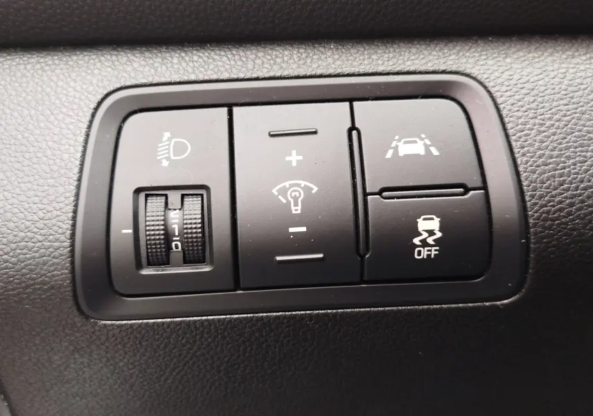Gros plan sur les commandes noires du tableau de bord de la Hyundai i20 2018, réglage phares et aides à la conduite.
