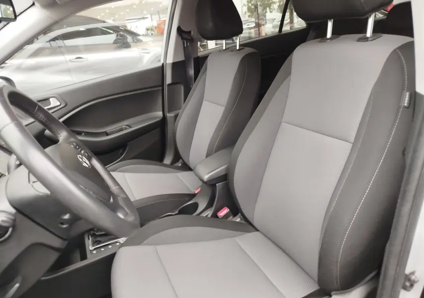Vue intérieure côté gauche de la Hyundai i20 2018, sièges tissu gris et volant avec commandes intégrées.