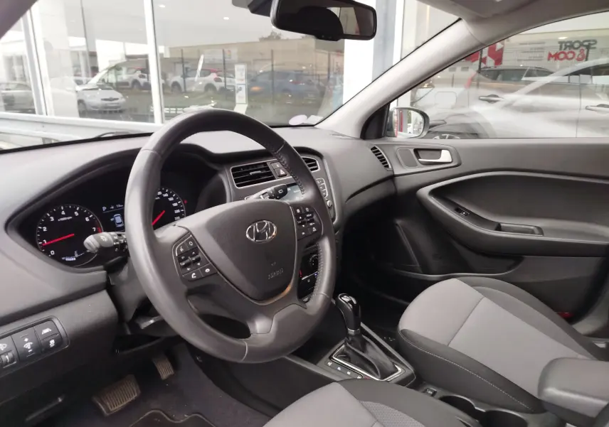 Vue intérieure côté conducteur de la Hyundai i20 2018 avec volant multifonction et sellerie tissu gris.