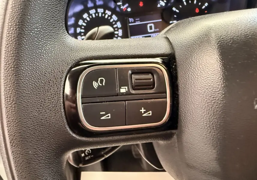 Gros plan sur les commandes du volant noir du Citroën Berlingo 2022, avec tableau de bord lumineux en arrière-plan.