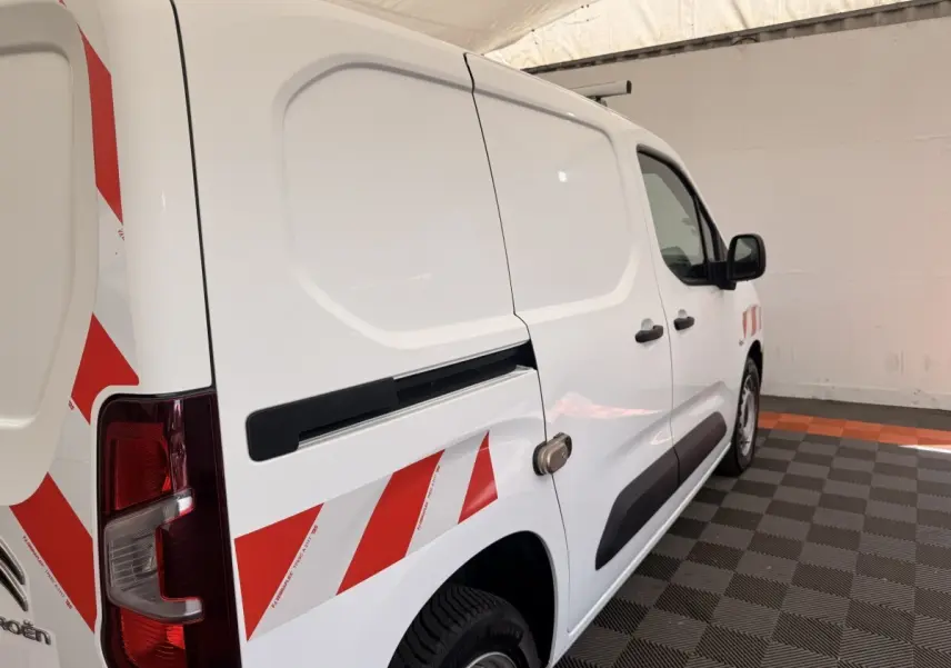 Vue 3/4 arrière droite d’un Citroën Berlingo blanc avec bandes rouges diagonales et porte latérale coulissante.