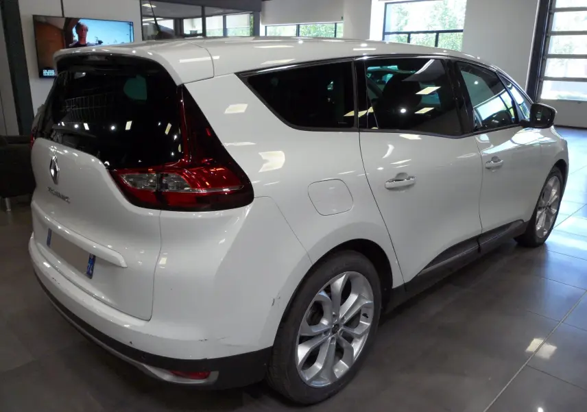 Vue 3/4 arrière droite d'un Renault Grand Scenic IV blanc Glacier en intérieur, avec vitres teintées et jantes alliage.