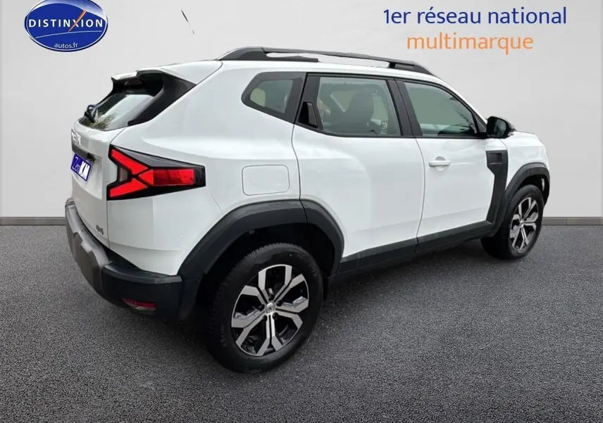 Vue 3/4 arrière droite d'un Dacia Duster blanc arctic 2025 avec barres de toit et feux arrière LED distinctifs.