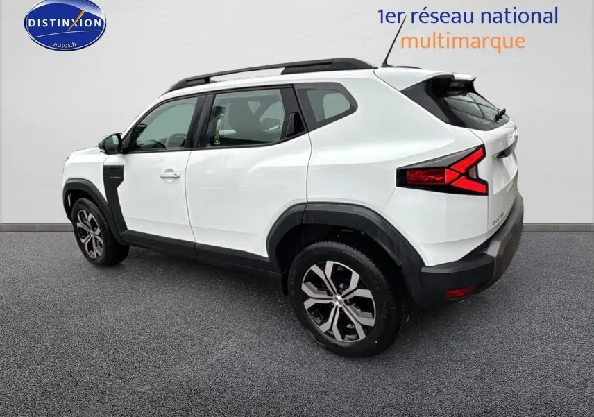 Vue 3/4 arrière droite du Dacia Duster blanc arctic 2025 avec jantes alu et barres de toit noires.