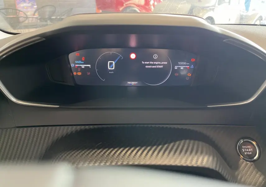 Vue rapprochée du tableau de bord numérique Peugeot 208 1.2 essence 2024 avec bouton start/stop et décor carbone.