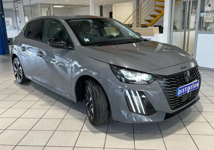 Peugeot 208 gris clair selenium vue 3/4 avant droit en showroom avec calandre noire et feux LED griffés.