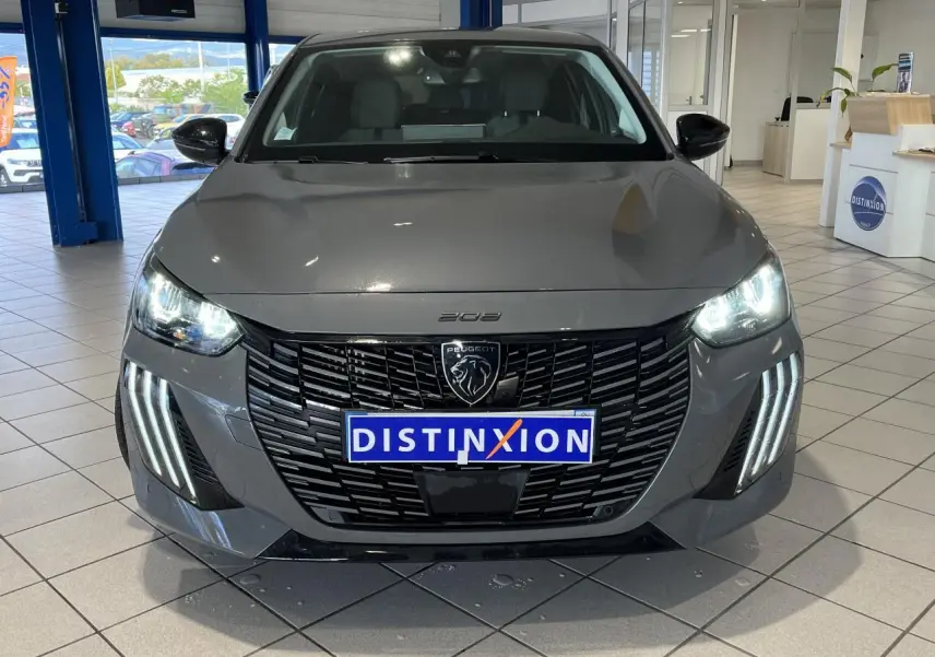 Vue avant d'une Peugeot 208 gris clair Selenium avec calandre noire et feux LED allumés en showroom.