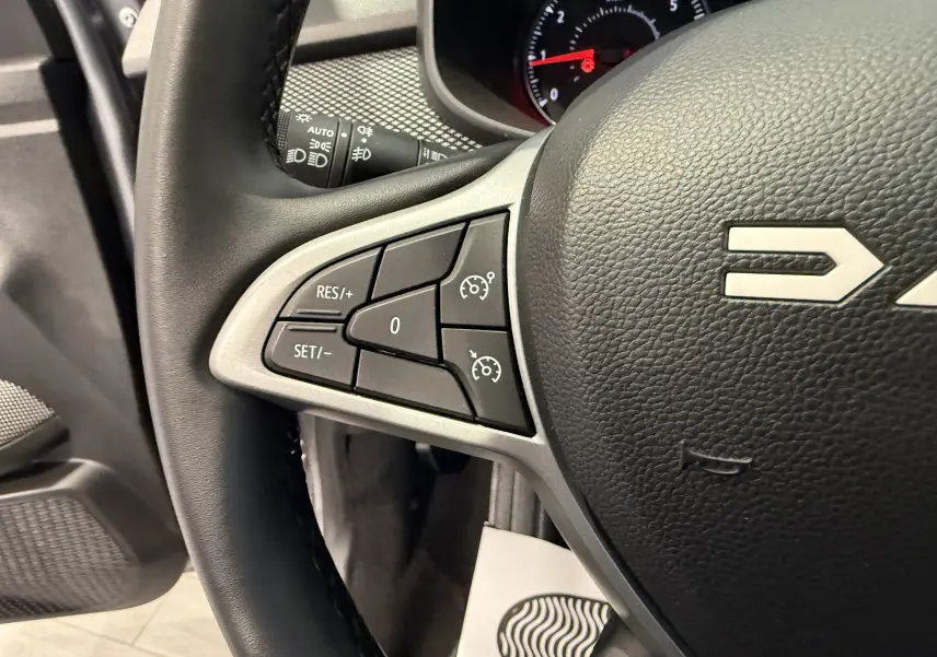 Gros plan sur le volant gris foncé de la Dacia Sandero 2025, montrant les commandes de régulateur de vitesse à gauche.