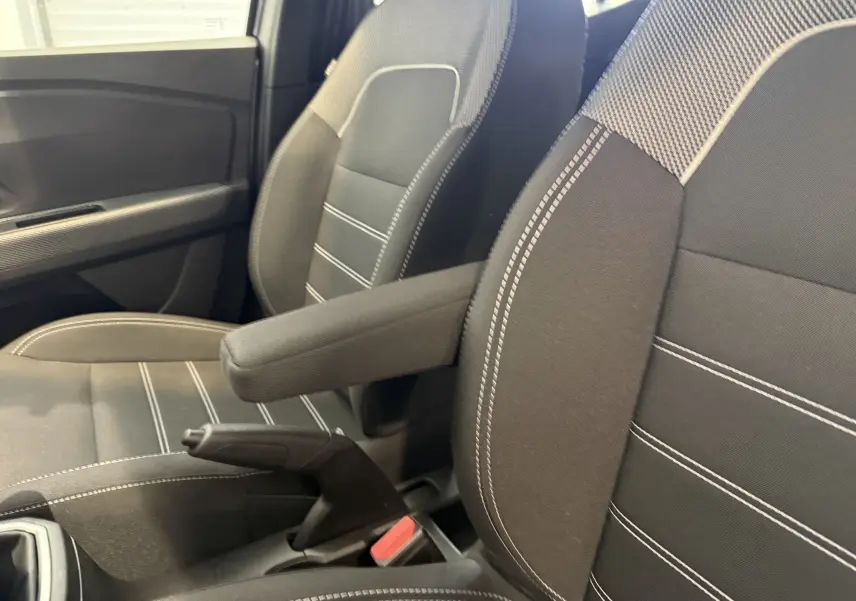 Gros plan sur les sièges avant gris avec accoudoir central et frein à main de la Dacia Sandero 2025.