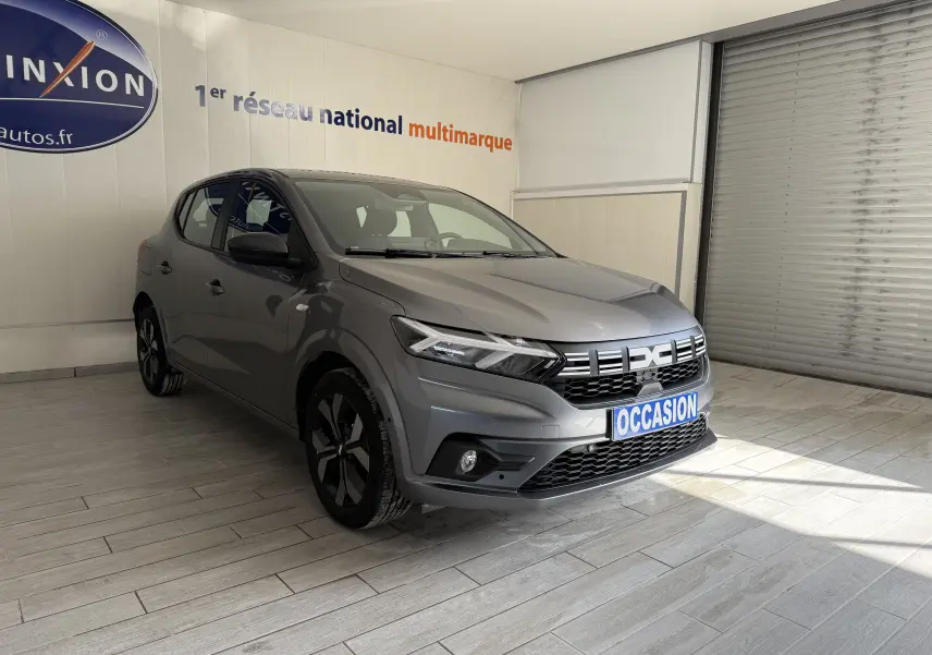 Dacia Sandero gris 2025 en 3/4 avant droit, avec calandre moderne et jantes noires distinctives.