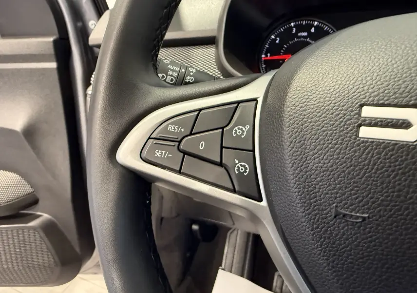 Gros plan sur les commandes de régulateur de vitesse au volant cuir noir de la Dacia Sandero 2025, côté gauche.